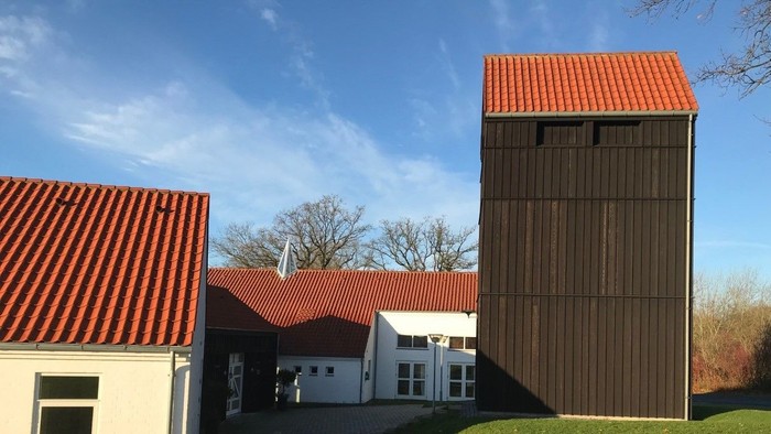 En lille gård med tre bygninger og røde tag, beliggende på en grøn ås