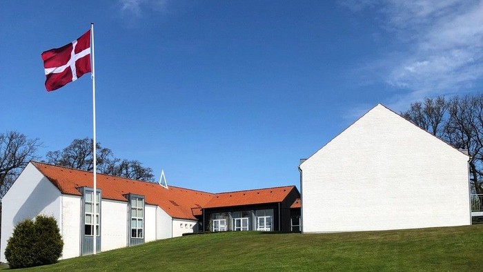 Hvid bygning med rødt tag og dansk flag på en bakke