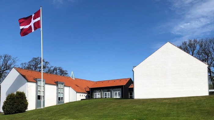 Hvidt hus med rødt tag og dansk flag på en bakke