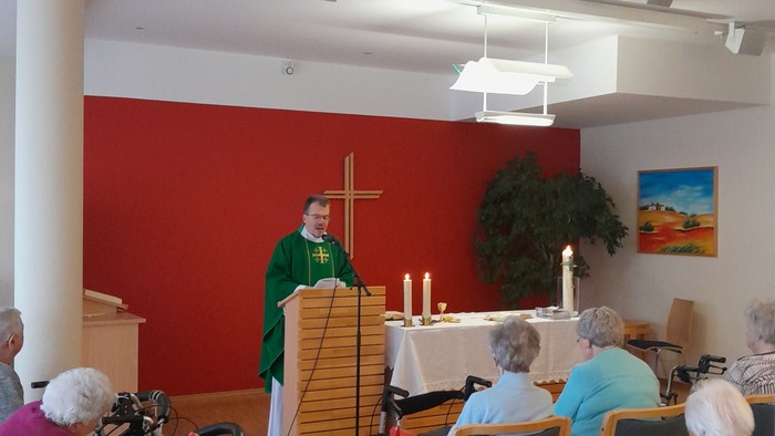 Ein Gottesdienst mit älteren Teilnehmern im Rollstuhl und einem Priester, der die Zeremonie leitet.