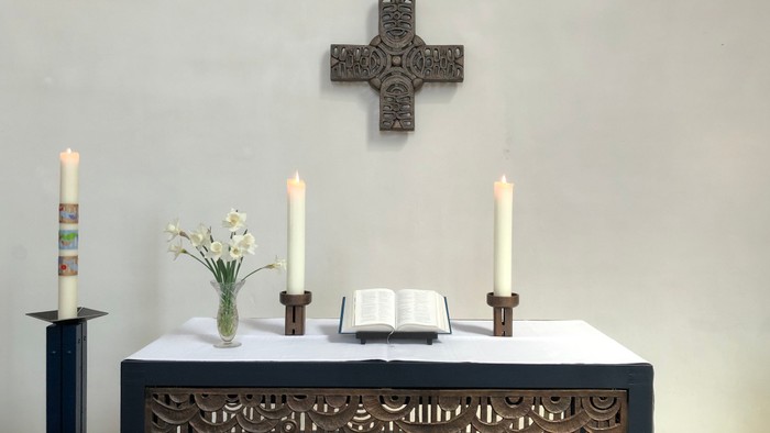 Ein Altar mit Kerzen, Blumen und einem Buch vor einem Kreuz an der Wand