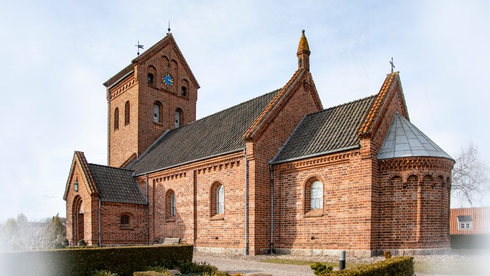 En lille kirke med teglmur og spåntagede tag, beliggende i en sovebygd.