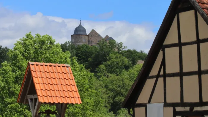 Eine Burg auf einem Hügel, umgeben von Bäumen, mit traditionellen Häusern im Vordergrund.
