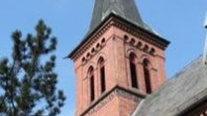 Das Bild zeigt einen Kirchturm aus rotem Backstein vor blauem Himmel.