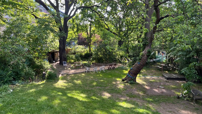 Üppiger Gartenbereich mit schattigen Sitzplätzen, umgeben von hohen Bäumen und Grün.