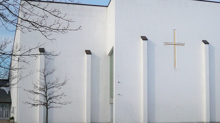 Moderne kirkefacade med et kors og noder, der symboliserer tilbedelse og harmoni.