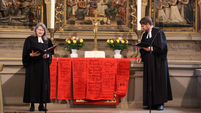 Zwei Priester stehen vor einem Altar mit Blumen und Kerzen.