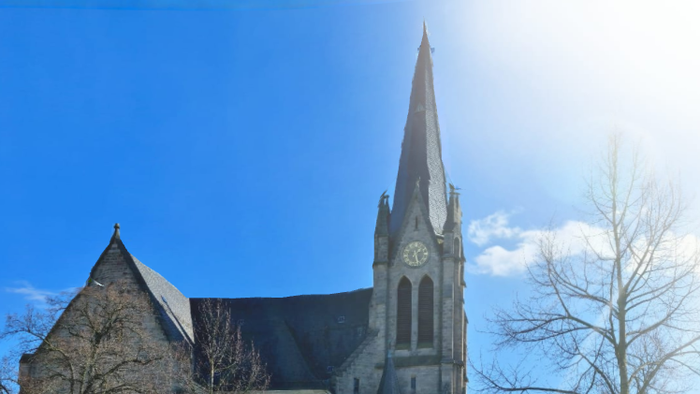 Kirche mit hohem Turmspitz und Uhr, umgeben von grünem Rasen und Blumen.