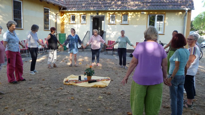 Eine Gruppe von Menschen, die sich an den Händen halten und einen Kreis um ein kleines Lagerfeuer oder eine Kerzenanordnung im Freien bilden.