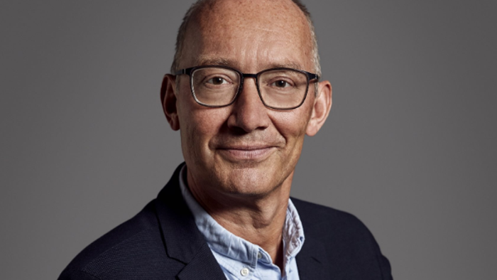 Professionel mand med briller, blazer og en lyseblå skjorte, der smiler til kameraet.