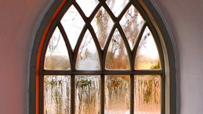 Et buevindue i en mur med udsigt over en sø og træer