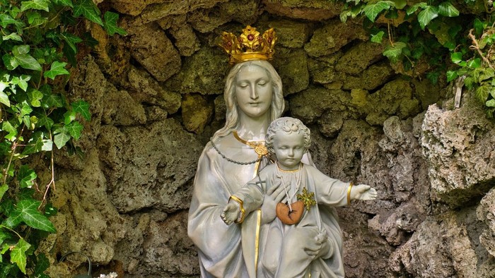Die Statue der Jungfrau Maria mit Baby Jesus vor Felswand.