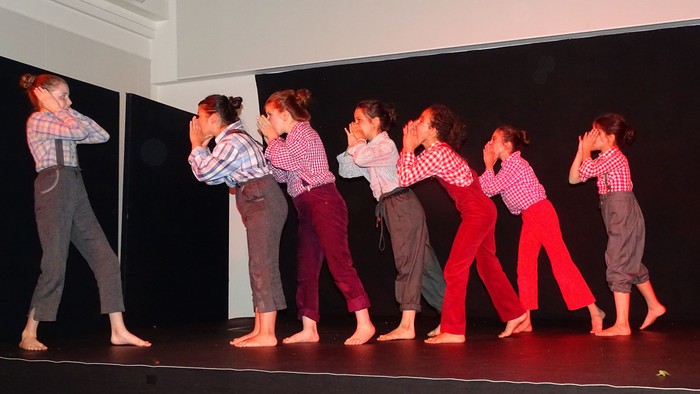 Eine Gruppe von Tänzerinnen in rosa Hemden und verschiedenen Hosen führt eine Choreographie auf einer Bühne auf