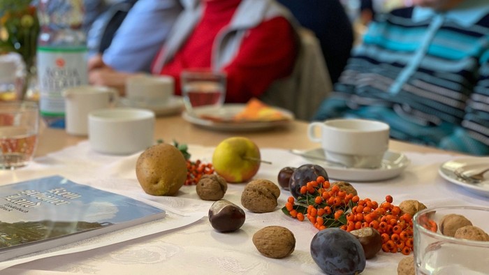 Ein festlicher Tisch mit verschiedenen Früchten, Nüssen und Menschen, die gemeinsam Getränke und Snacks genießen.