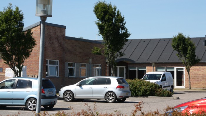 En parkeringstomt med flere biler og et mørkt teglsteinsbygning.