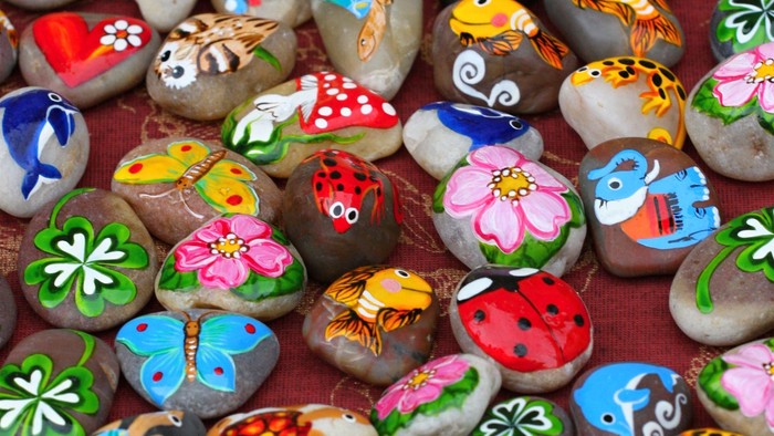 Billedet viser malede sten med forskellige motivet som blomster, dyr og patterner.