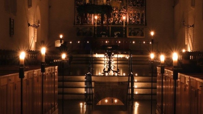 En kirkeindgang belyset af talrige lysestake.