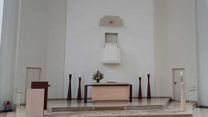 Minimalistischer Kirchenaltar mit schlichten Holzmöbeln und einer zentralen Blumendekoration unter einem Sternenemblem.