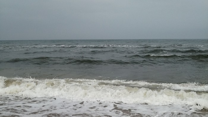 Strand mit Wellen und bewölktem Himmel