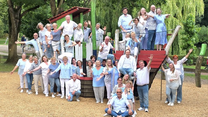 Gruppe von Menschen in passenden Outfits, die fröhlich auf einem Spielplatz mit Klettergerüsten posieren.