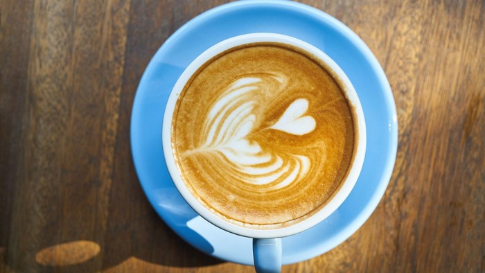 Eine Tasse Kaffee mit Herz- und Blattmuster auf einem Holztisch.