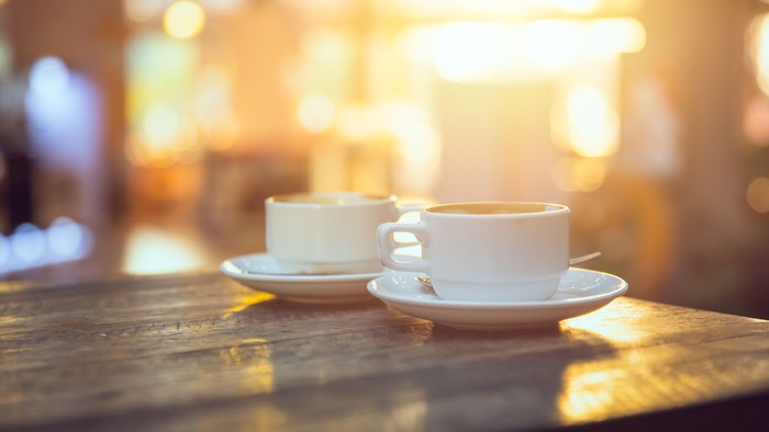 Zwei weiße Tassen mit Untertassen auf einem Holztisch bei Sonnenlicht