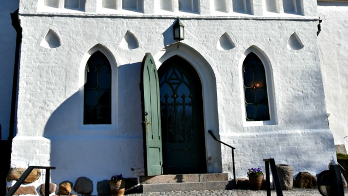 Et hvidt kirkeportal med grøn dør og smukke buevinduer