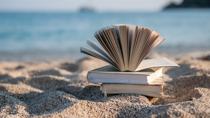 Ein aufgeschlagenes Buch liegt auf einem Sandstrand am Meer.