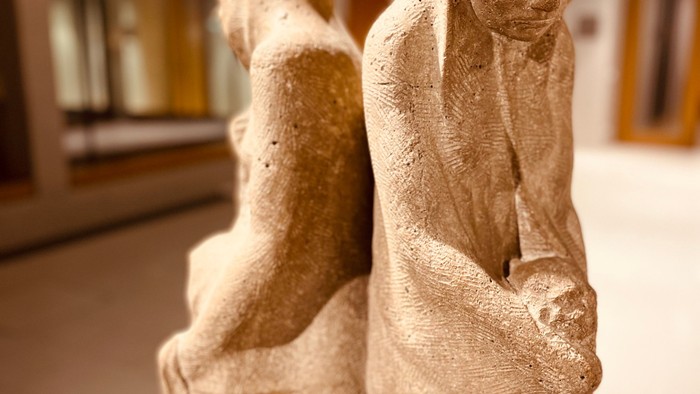 Zarte Steinskulptur einer Mutter, die ein Kind in einer ruhigen Innenraumeinstellung wiegt.