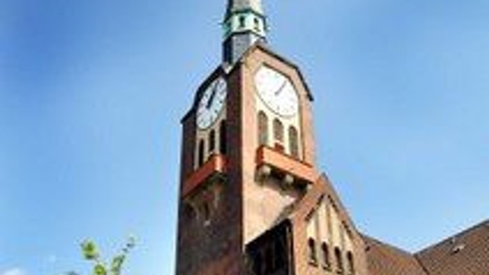 Eine markante Backsteinkirche mit hohem Kirchturm und Uhrturm vor einem klaren blauen Himmel.