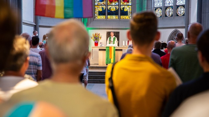 Menschen versammeln sich in einer Kirche mit bunten Fahnen.