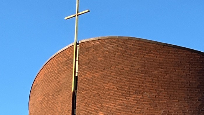 En stor mørk murstenskirke med et guldæret kors på toppen.