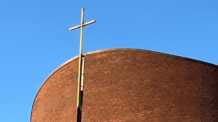 En stor mørk murstenskirke med et guldæret kors på toppen.
