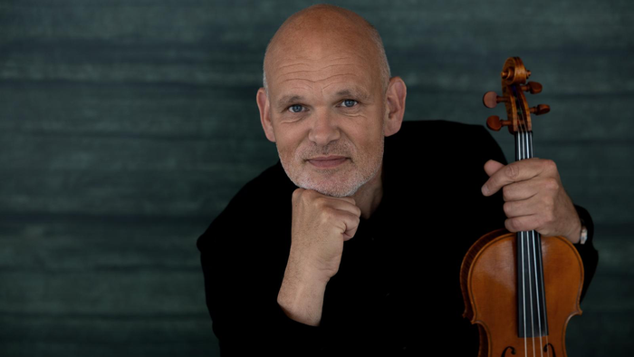 En skaldet mand i sort tøj holder en violin og smiler.
