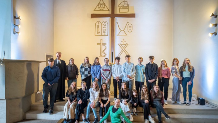 Gruppe junger Menschen, die in einer Kirche mit religiösen Symbolen an der Wand posieren.