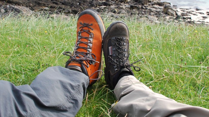 Beine mit Wanderschuhen auf einer grünen Wiese mit Felsen am Meer