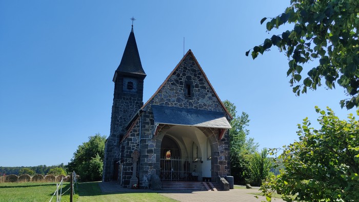 Kleine Kirche mit Turm und Kreuz vor grünem Hintergrund