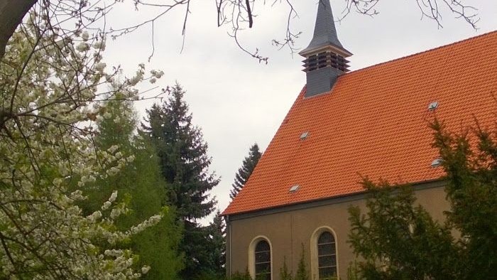 Eine malerische Kirche mit einem orangen Ziegeldach und einem Kirchturm, eingerahmt von blühenden Bäumen und Grün.