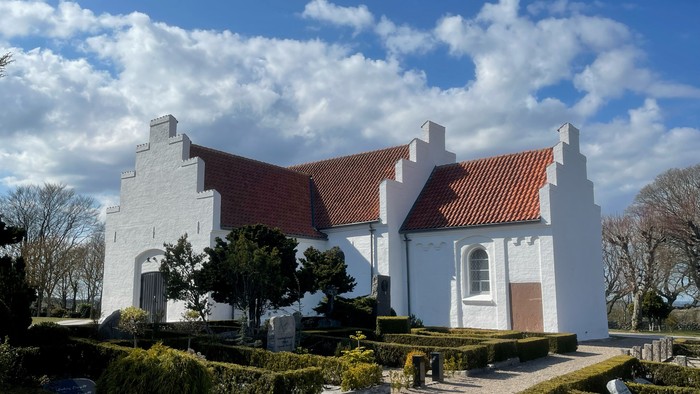 Et hvidt præstegård med røde tag og omgivelser med buske og træer