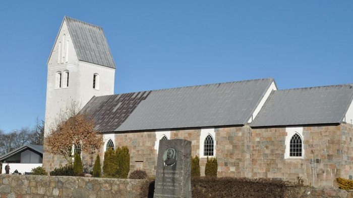 En lille kirke med tårn og lavt tag i en landsby.