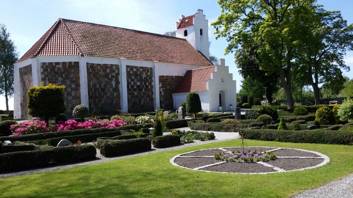 En smuk havescene med en lille kirke og farverige blomsterbænker