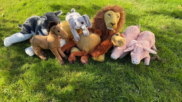 En farverig gruppe af tøjdyr, herunder en løve, elefanter, en hest og en hund, der sidder på græsset.