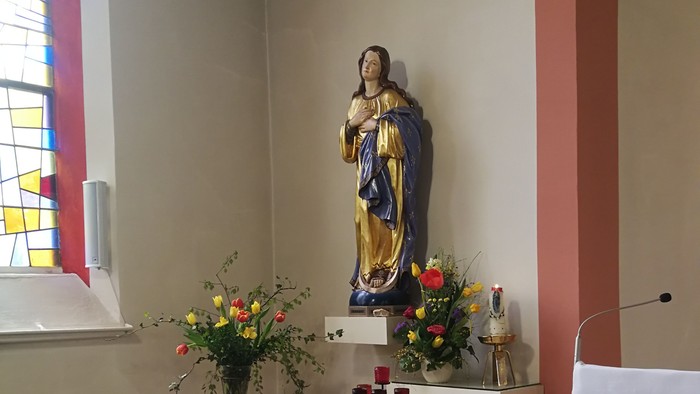 In der Kirche steht eine Statue der Jungfrau Maria mit Blumen und Kerzen.
