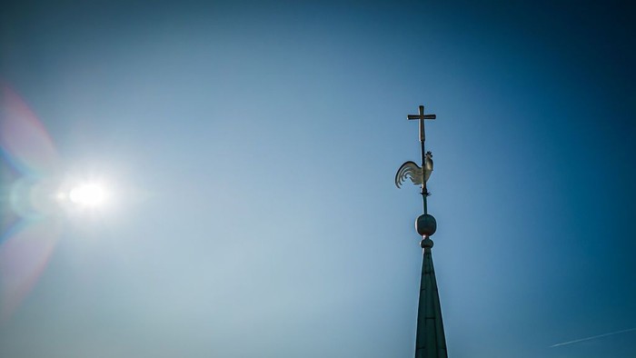 Vejrhane på toppen af et spir mod en klar, lysende himmel.