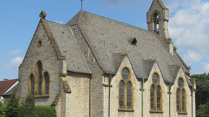 Historische Steinkirche mit steilem Dach, spitzen Fenstern und einem kleinen Glockenturm unter klarem Himmel.