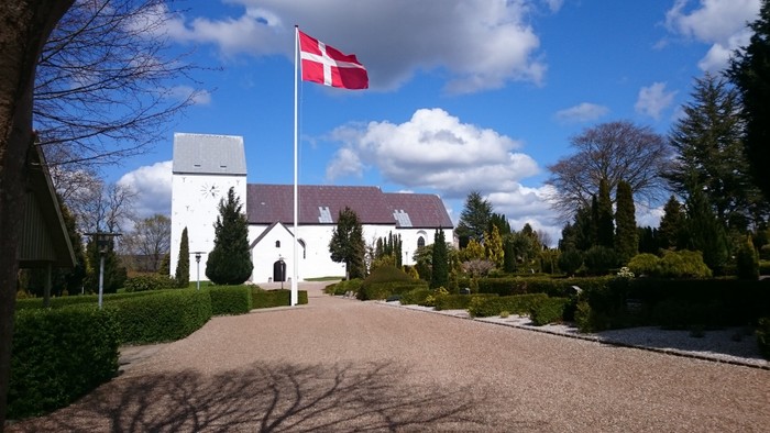 En hvid kirke med dansk flag på en solskinnede dag