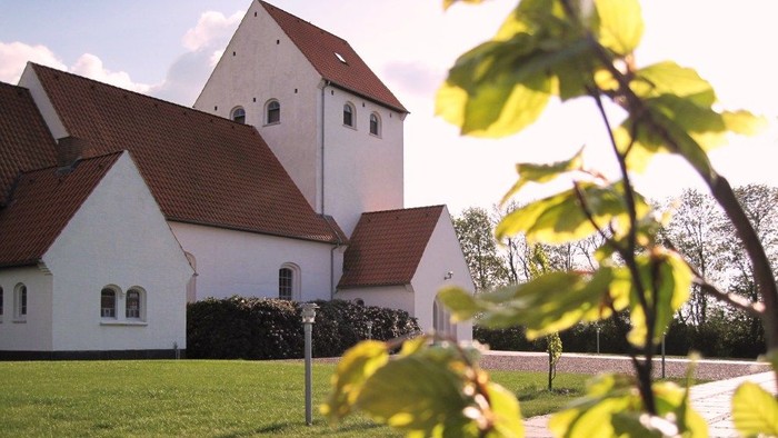 En hvid kirke med røde tag og en grøn have foran