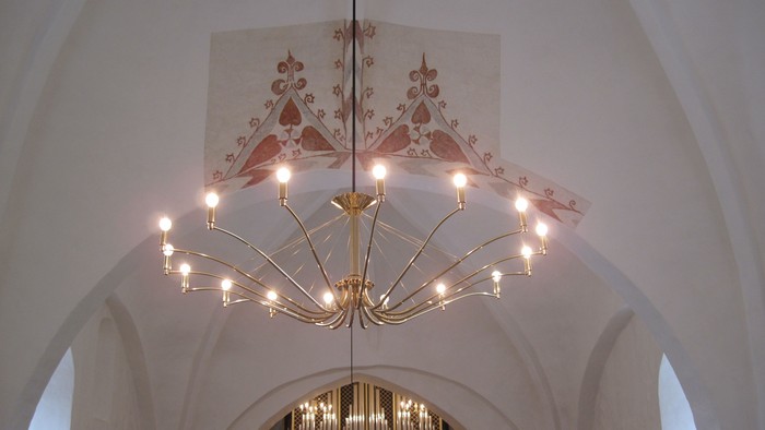 Stor lyskærm hænger i hvidt tårn med malet dekoration.