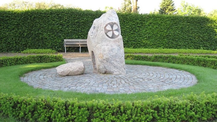 En sten med symboldragning i en park med benk og buske