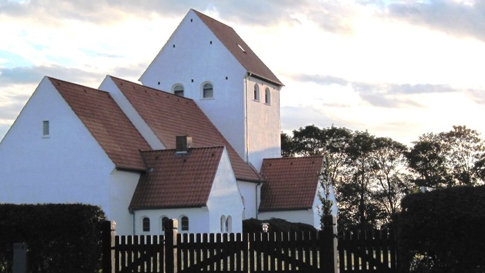 Et hvidt og rødt taget hus med en mur og træer i forgrunden